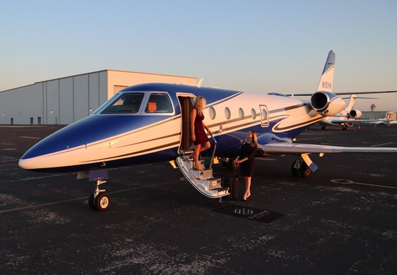 Female passenger disembarking from private jet with flight attendant greeting her at the bottom of the steps.