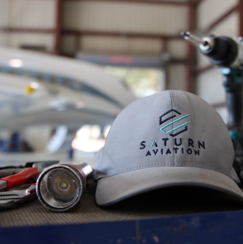 Workbench with tools and a Saturn Aviation hat on it with jet in the background
